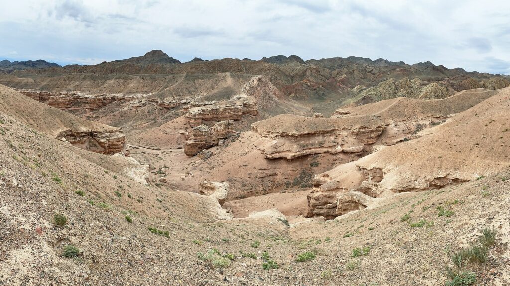 Eroded sandstone formations and dry valleys of Charyn Canyon, Kazakhstan, under a cloudy sky.