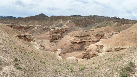 Eroded sandstone formations and dry valleys of Charyn Canyon, Kazakhstan, under a cloudy sky.