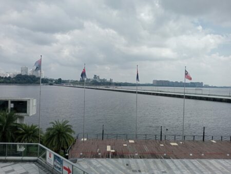 Johor-Singapore Causeway seen across the water from the Malaysian side, with flags on poles in the foreground