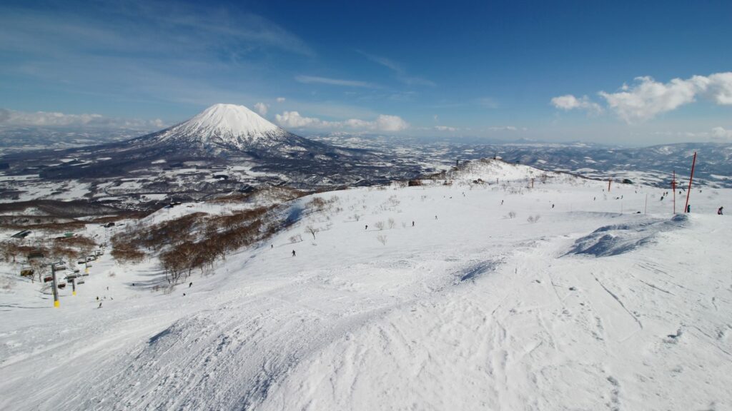 Snowy ski slope in Niseko with snow-capped Mount Yotei rising under a blue sky in the distance