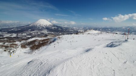 Snowy ski slope in Niseko with snow-capped Mount Yotei rising under a blue sky in the distance