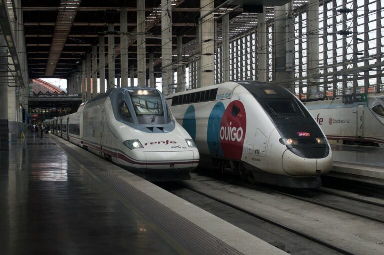 A Renfe AVE high-speed train beside an OUIGO double-deck TGV at Madrid Puerta de Atocha station in Spain