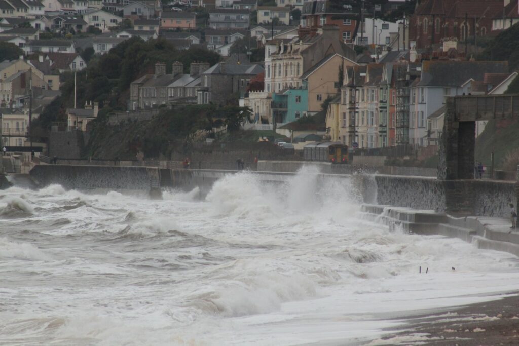 Storm waves crash over the sea wall at Dawlish in Devon as a passenger train passes along the coastal railway