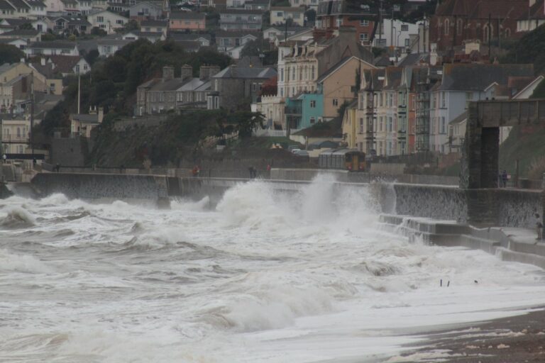 Storm waves crash over the sea wall at Dawlish in Devon as a passenger train passes along the coastal railway