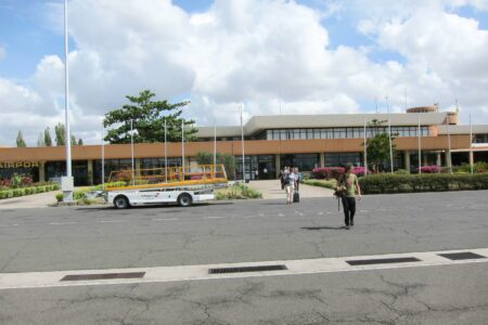 The terminal building at Kilimanjaro International Airport in Tanzania under a partly cloudy sky, with a few travellers walking across the apron