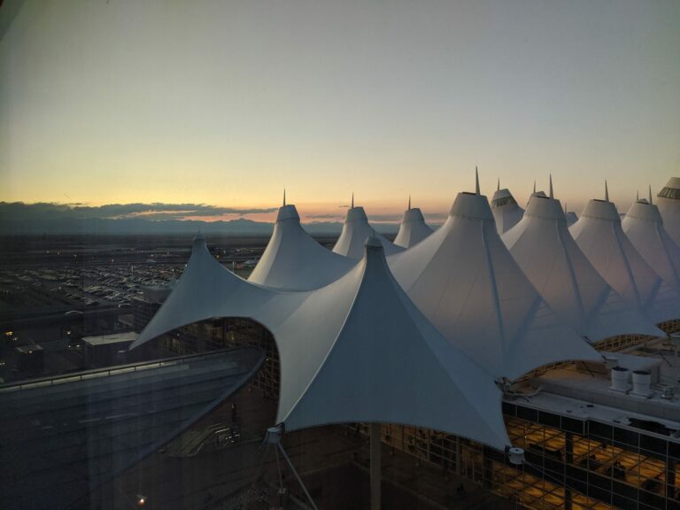 White peaked roof of Denver International Airport main terminal at dusk, with a glowing sky over the horizon