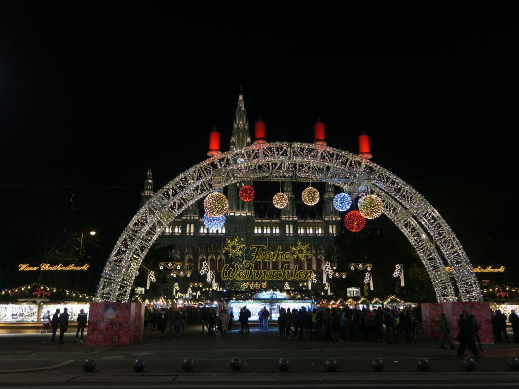 Illuminated arch and Christmas market stalls in front of Vienna City Hall at dusk