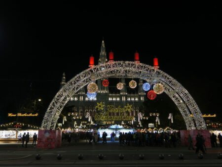 Illuminated arch and Christmas market stalls in front of Vienna City Hall at dusk